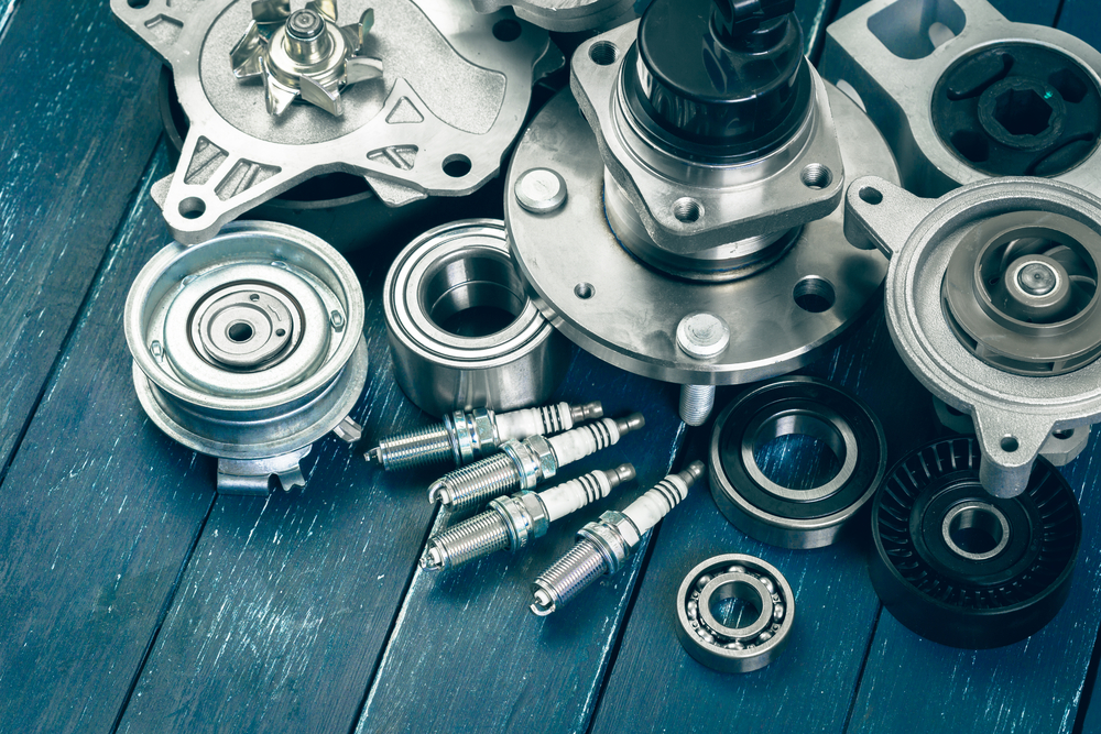 Assortment of automotive replacement parts, including spark plugs, bearings, pulleys, and water pumps, arranged on a workbench.