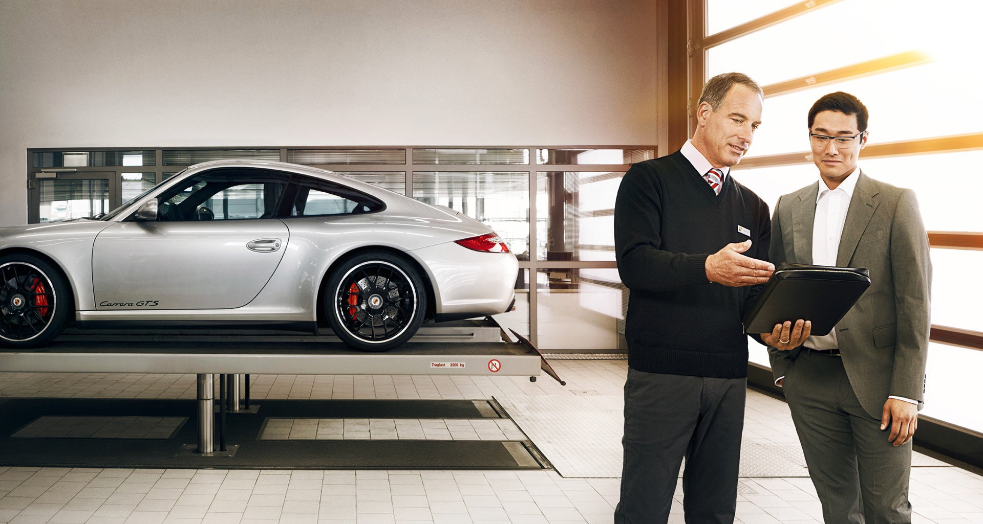 A Porsche Certified Service Technician discussing Performance Vehicle Service options with customers and a Porsche vehicle in the background